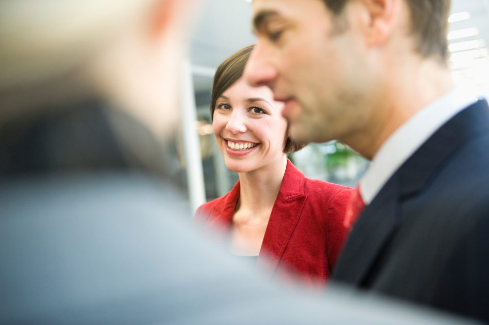 Femme souriante en blazer rouge discutant avec un homme en costume dans un bureau moderne