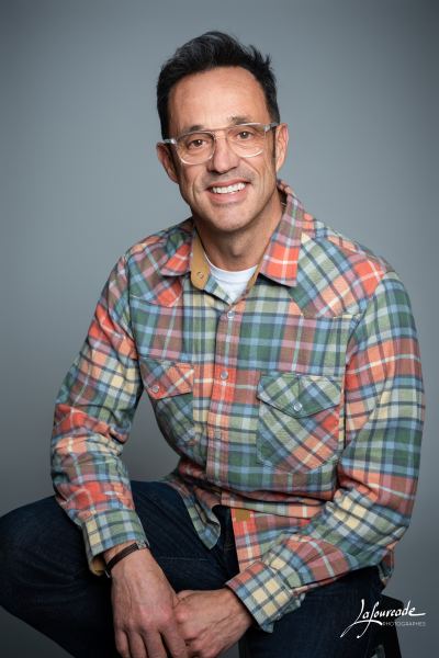 Homme souriant assis dcontract, portant une chemise  carreaux colore et des lunettes fines